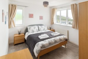 Ein Schlafzimmer mit Bett, Nachttischen, einer Lampe und Blick ins Freie.