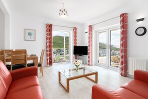 A modern living room with a sofa, a coffee table, a TV, and a dining area with chairs and a table. - Sunnycliffe House (Woolacombe)
