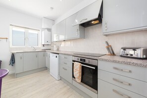 A modern kitchen with white cabinets, a built-in oven, and a toaster. - Sunnycliffe House (Woolacombe)