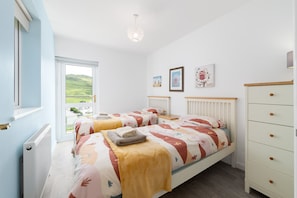 A bedroom with two beds, a dresser, and a window with a view of greenery. - Sunnycliffe House (Woolacombe)