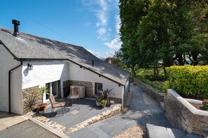A house with a stone exterior, a tiled roof, and a paved patio with outdoor furniture. - Courtyard Cottage, Barnstaple (Barnstaple)