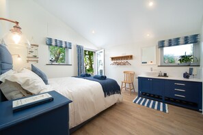 A bedroom with a bed, bedside table, lamp, and a view of greenery outside. - Courtyard Cottage, Barnstaple (Barnstaple)
