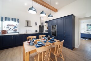 A modern kitchen with dark blue cabinets, a wooden dining table, and pendant lighting. - Courtyard Cottage, Barnstaple (Barnstaple)