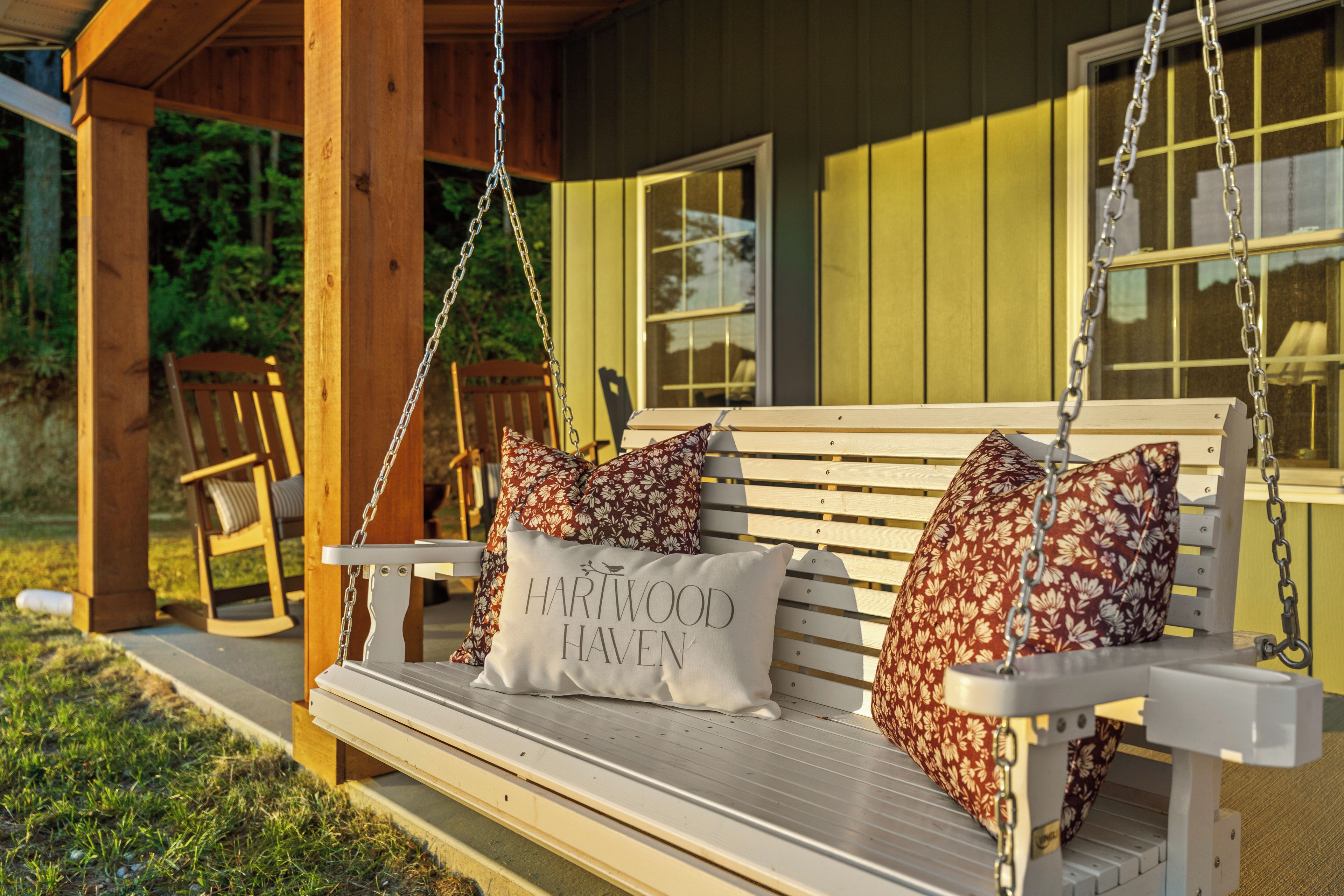 A wooden swing bench with floral cushions and a cushion with 'HARTWOOD HAVEN' text.