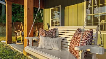 A wooden swing bench with floral cushions and a cushion with 'HARTWOOD HAVEN' text.