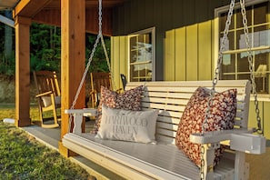 A wooden swing bench with floral cushions and a cushion with 'HARTWOOD HAVEN' text. - Woodland Retreat - Near Ash Cave - Hot Tub, Sauna, Game Room (Laurelville)