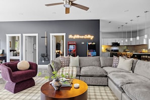 A modern living room with a grey sofa, a purple armchair, and a coffee table with a vase. - Woodland Retreat - Near Ash Cave - Hot Tub, Sauna, Game Room (Laurelville)