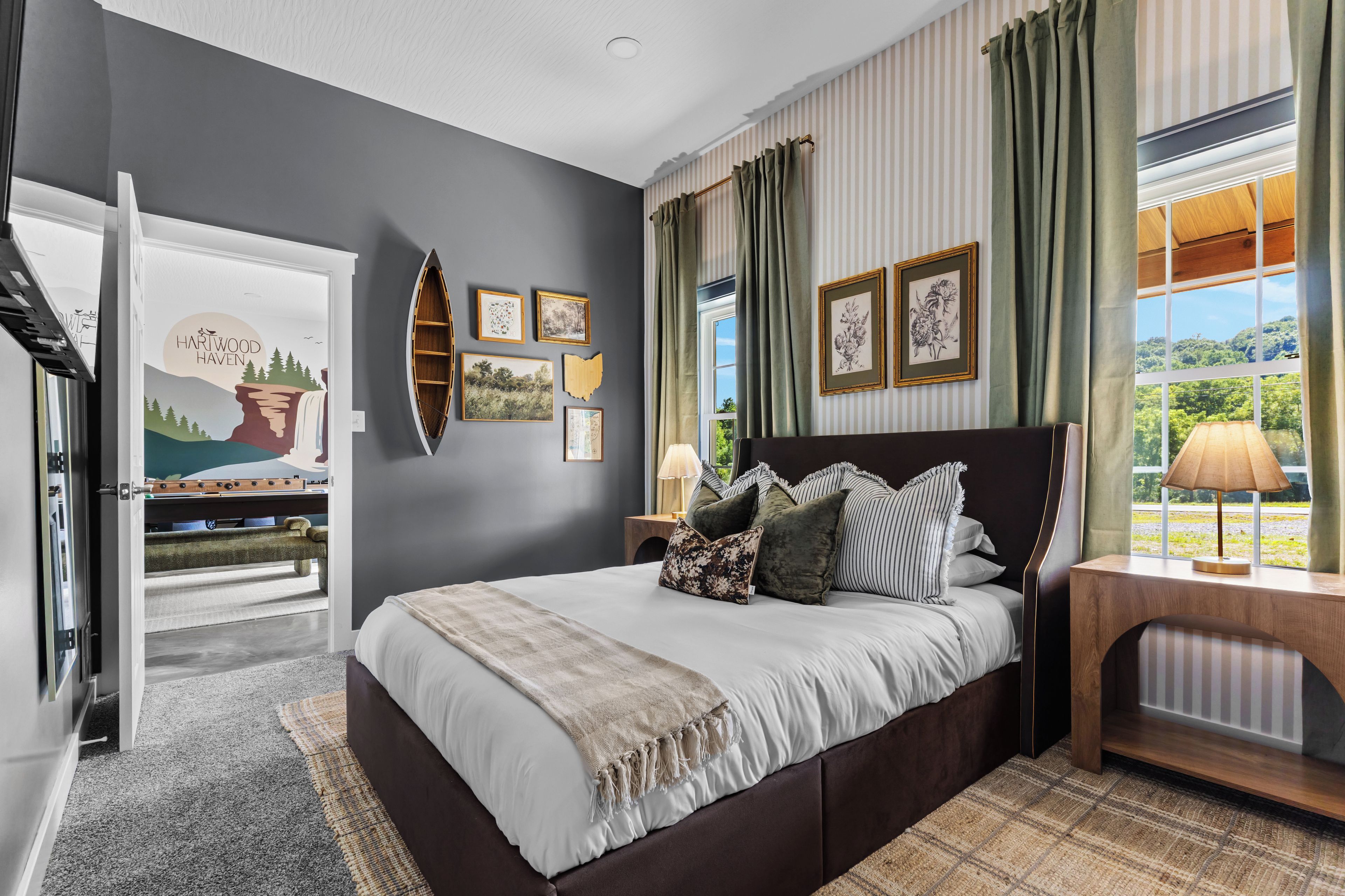 Une chambre à coucher avec un lit, une table de chevet, une fenêtre avec des rideaux et des œuvres d’art murales.