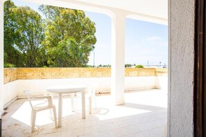 An outdoor patio with a table and chairs, a stone wall, and trees in the background. - Apartment 'Residence Eriguez - 1' with Sea View, Wi-Fi and Air Conditioning (Marina di Mancaversa)
