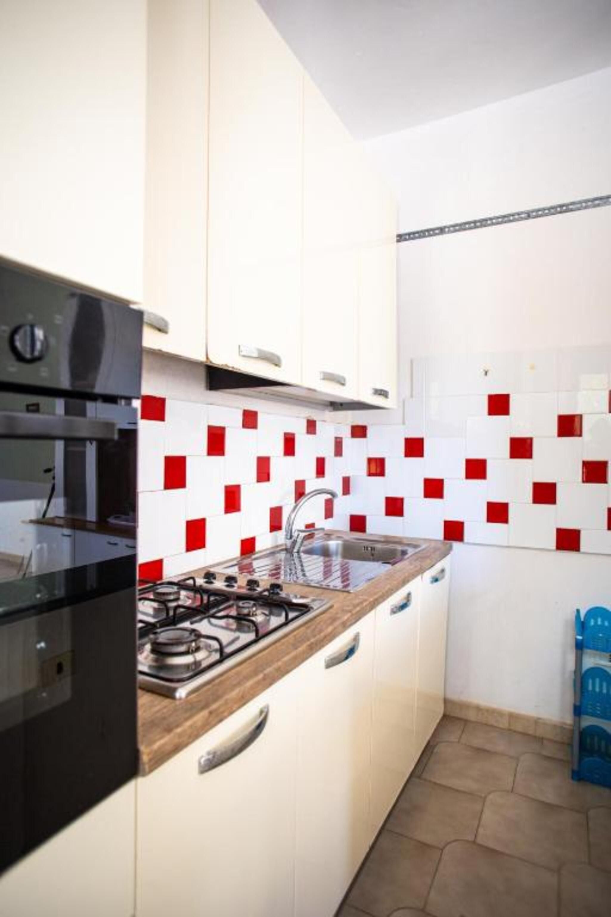 Una cocina con armarios blancos, estufa a gas y salpicadero con azulejos rojos y blancos.