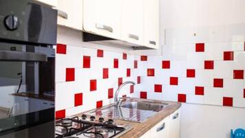 Una cocina con armarios blancos, estufa a gas y salpicadero con azulejos rojos y blancos.