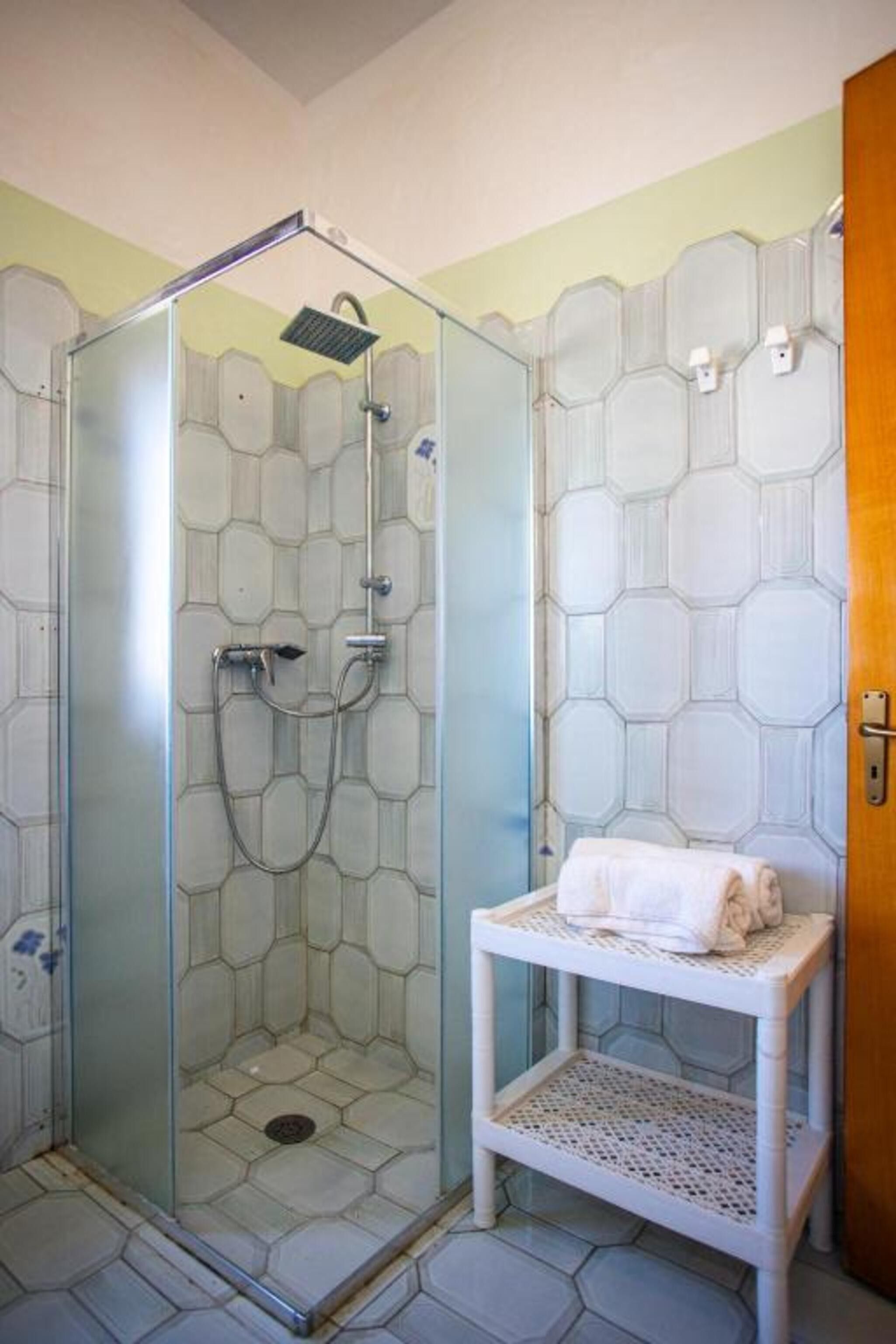 Eine Dusche mit Glastür, ein weißes Handtuch auf einer Ablage und Wände mit sechseckigem Muster.