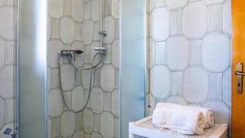 Eine Dusche mit Glastür, ein weißes Handtuch auf einer Ablage und Wände mit sechseckigem Muster.
