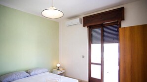 Quarto com cama, mesa de cabeceira, luminária e janela com persianas.