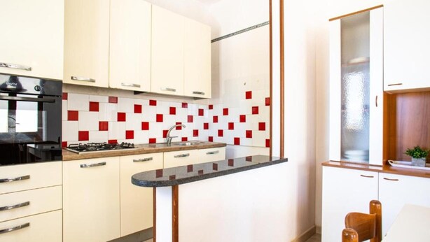 Cozinha moderna com armários brancos, bancada preta e azulejos vermelhos quadrados na parede do fundo.