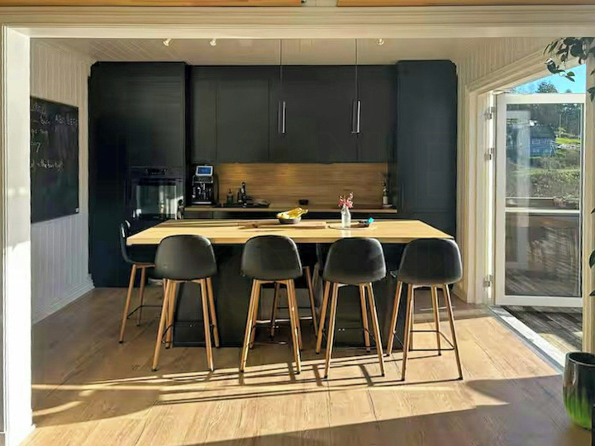 A modern kitchen with a central island, black cabinets, and wooden stools.