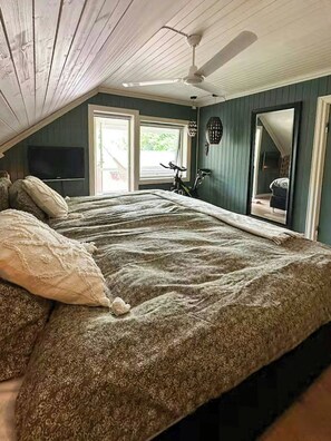 A bedroom with a large bed, a ceiling fan, and a view of the outdoors.
