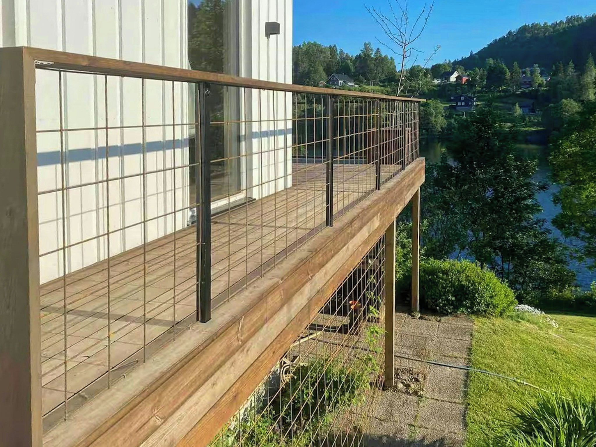 Eine Holzterrasse mit Metallgeländer, die auf ein Gewässer und einen Hügel blickt.