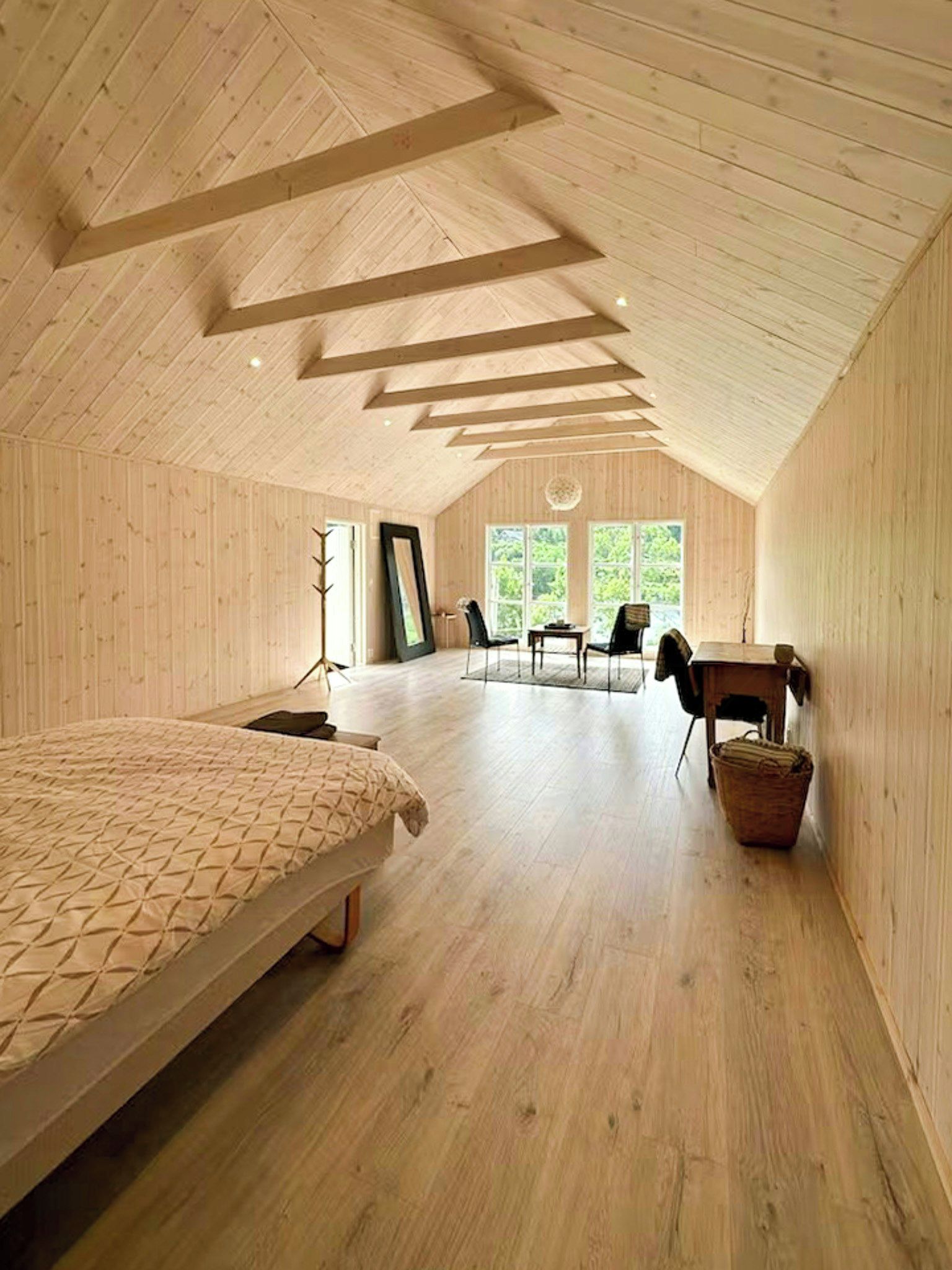 A spacious attic bedroom with a large bed, a desk, and a chair.