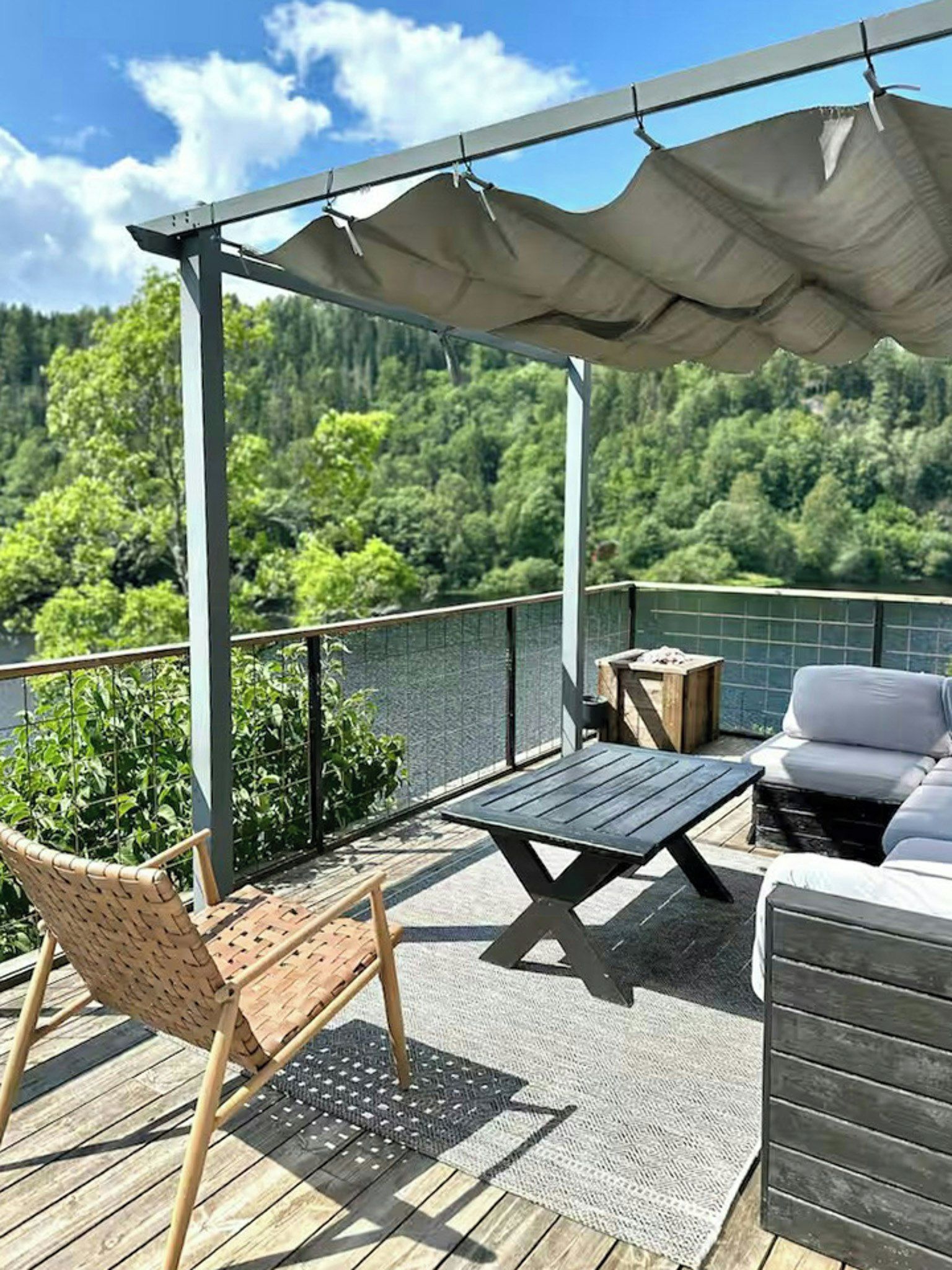 Una terraza con una pérgola, mobiliario exterior y vistas a un paisaje boscoso.