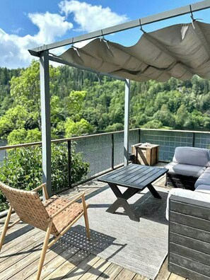 Una terraza con una pérgola, mobiliario exterior y vistas a un paisaje boscoso.
