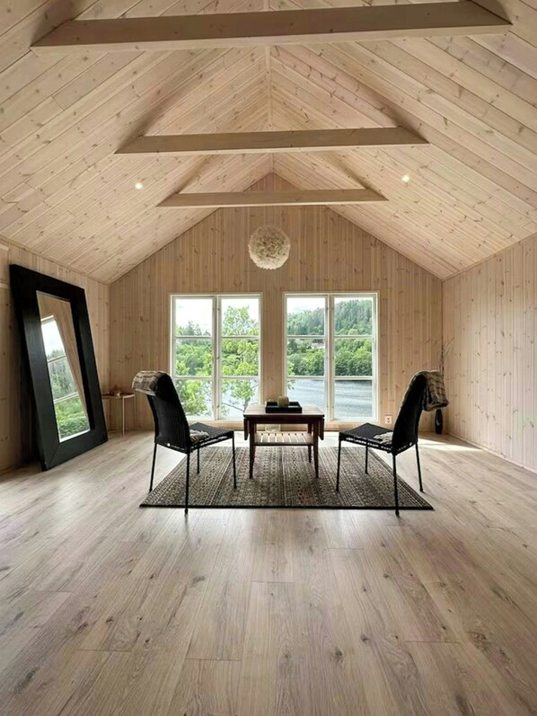 A spacious room with a high ceiling, large windows, and a view of a lake.