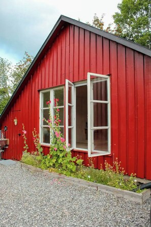 A red building with a white-framed window and a flower box with pink flowers.
