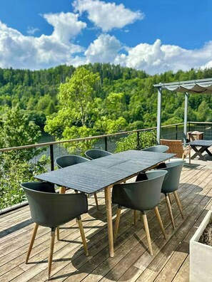 An outdoor deck with a table and chairs, overlooking a forested landscape.