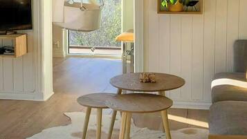 A room with a television, a hanging chair, a round table with stools, a cowhide rug, and a shelf with decorative items.