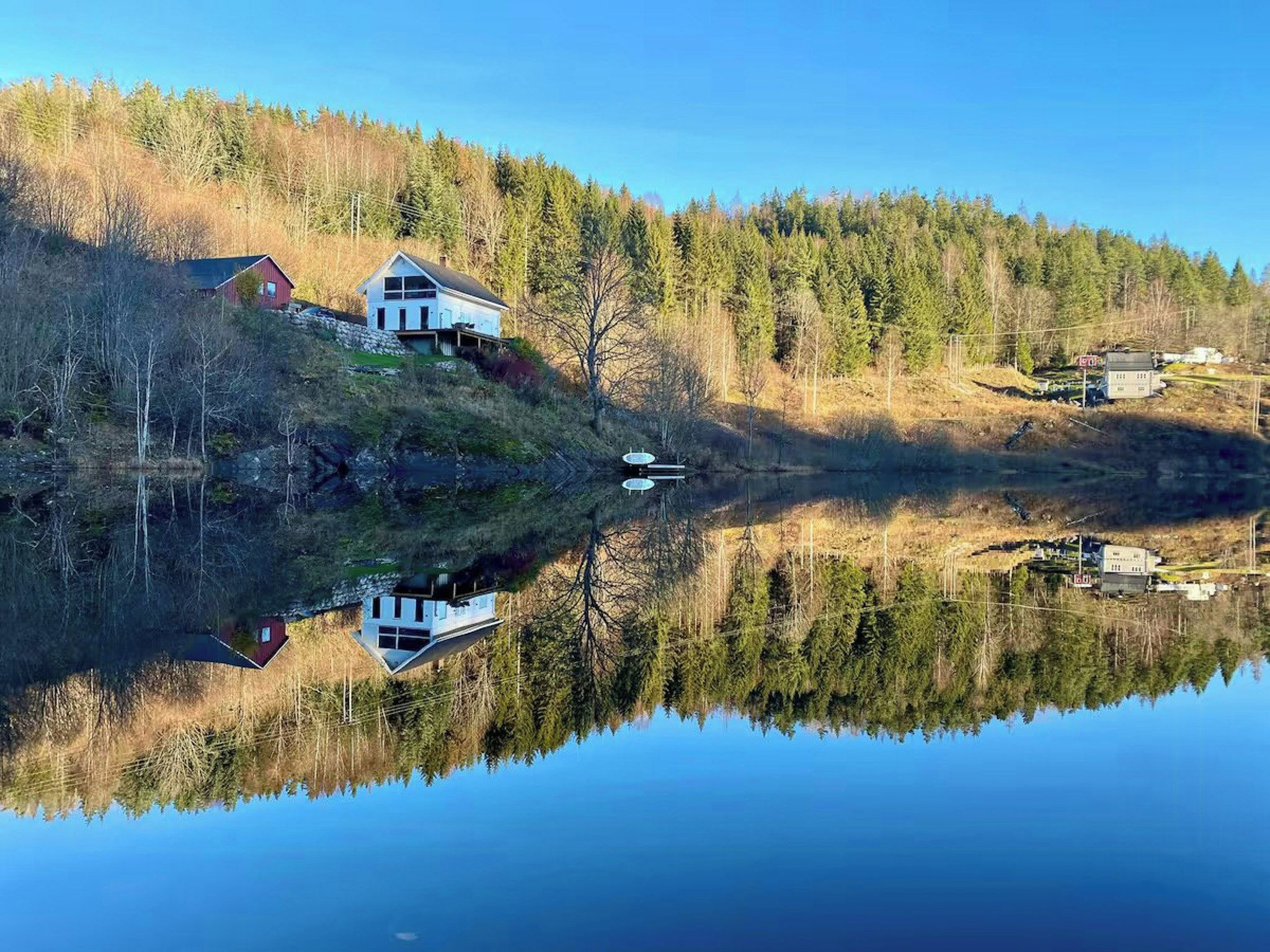 Eine friedliche Seenlandschaft mit einem Haus, das sich im Wasser spiegelt, umgeben von dichtem Wald.