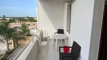 Ein Balkon mit einem weißen Tisch, zwei Stühlen und einem schwarzen Sessel.