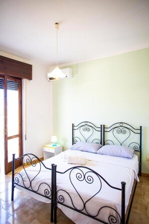 A bedroom with a bed, a nightstand, a lamp, and a window with blinds. - Apartment 'Residence Eriguez - 2' with Shared Pool, Wi-Fi and Air Conditioning (Marina di Mancaversa)