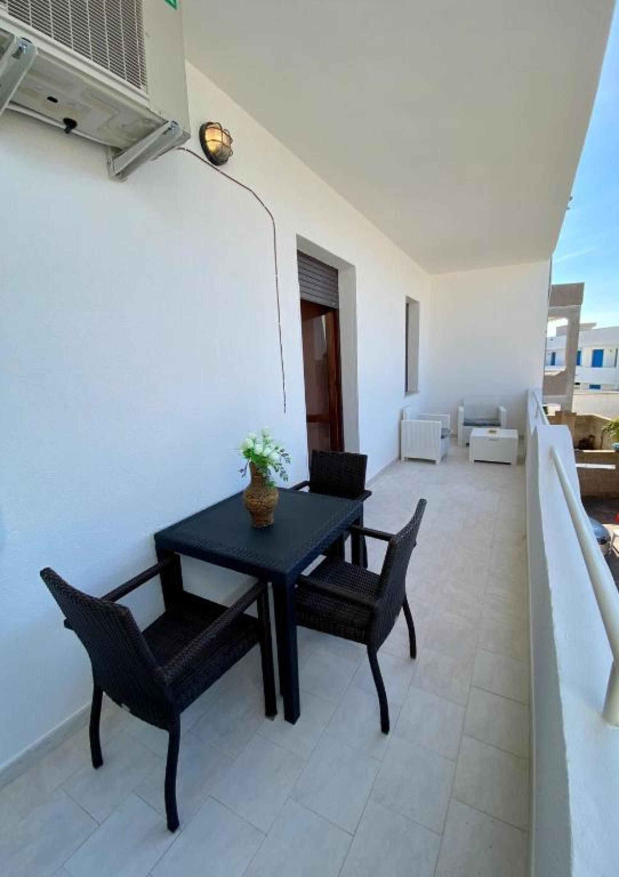A balcony with a table and chairs, a potted plant, and a white radiator.