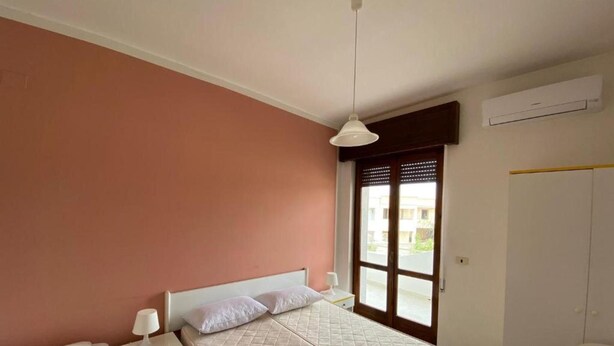 Quarto com cama, mesas de cabeceira, guarda-roupa e janela com vista.