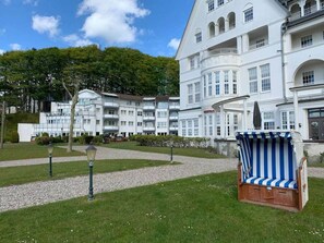 A hotel with a white facade, multiple balconies, and a garden area with a striped chair. - Villa Mare Sea View (Gluecksburg)