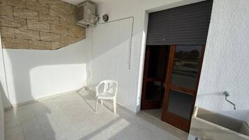 Un balcó amb una paret de pedra, una cadira blanca i una porta corredissa de vidre.