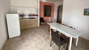 Cozinha compacta com geladeira, mesa de jantar com cadeiras e janela com vista.