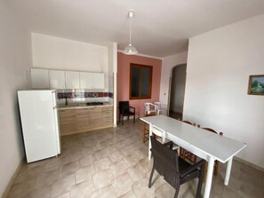 A compact kitchen with a refrigerator, a dining table with chairs, and a window with a view. - Apartment 'Residence Eriguez - 4' with Sea View, Wi-Fi and Air Conditioning (Marina di Mancaversa)