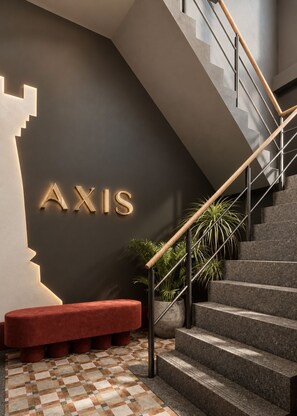 A modern staircase with a wooden handrail and metal balusters, leading to a dark wall with illuminated letters spelling 'AXIS'. - Axis.Bangkok Chess (Bangkok)