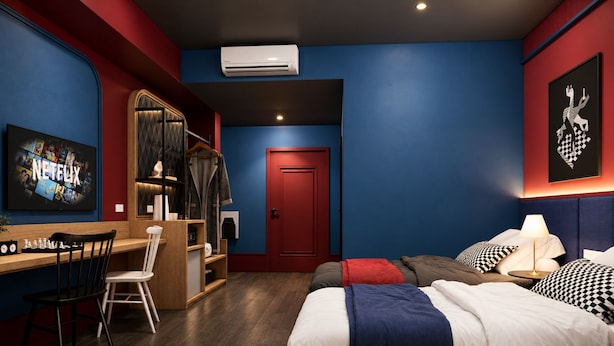 Habitación de hotel con escritorio, una silla, una cama con varias almohadas, armario y una puerta.