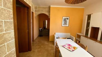A room with a stone wall, a wooden door, a dining table with chairs, a white cabinet, and a ceiling light fixture.
