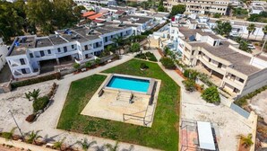 Ett bostadsområde med en swimmingpool omgiven av en gräsmatta, beläget intill högre byggnader.