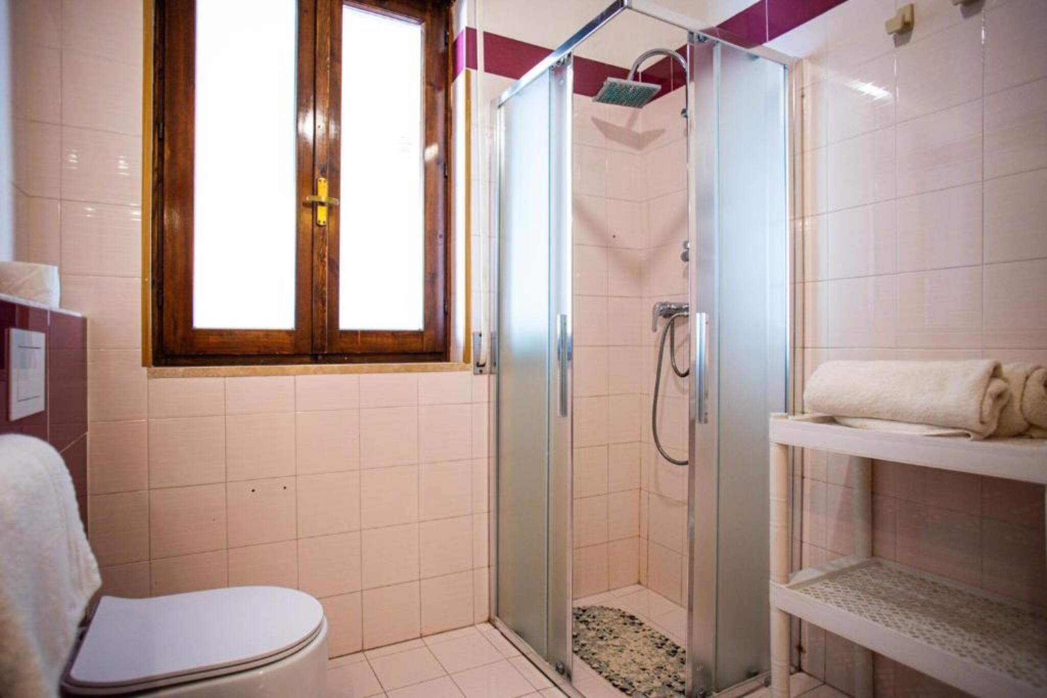 A bathroom with a glass-enclosed shower, a toilet, and a shelf with towels.