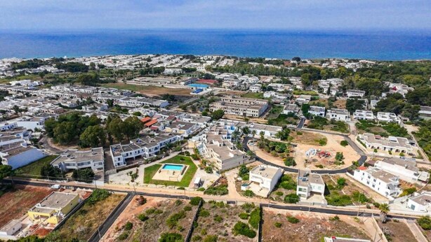 Vista aérea de uma área residencial costeira com casas, ruas e uma piscina.