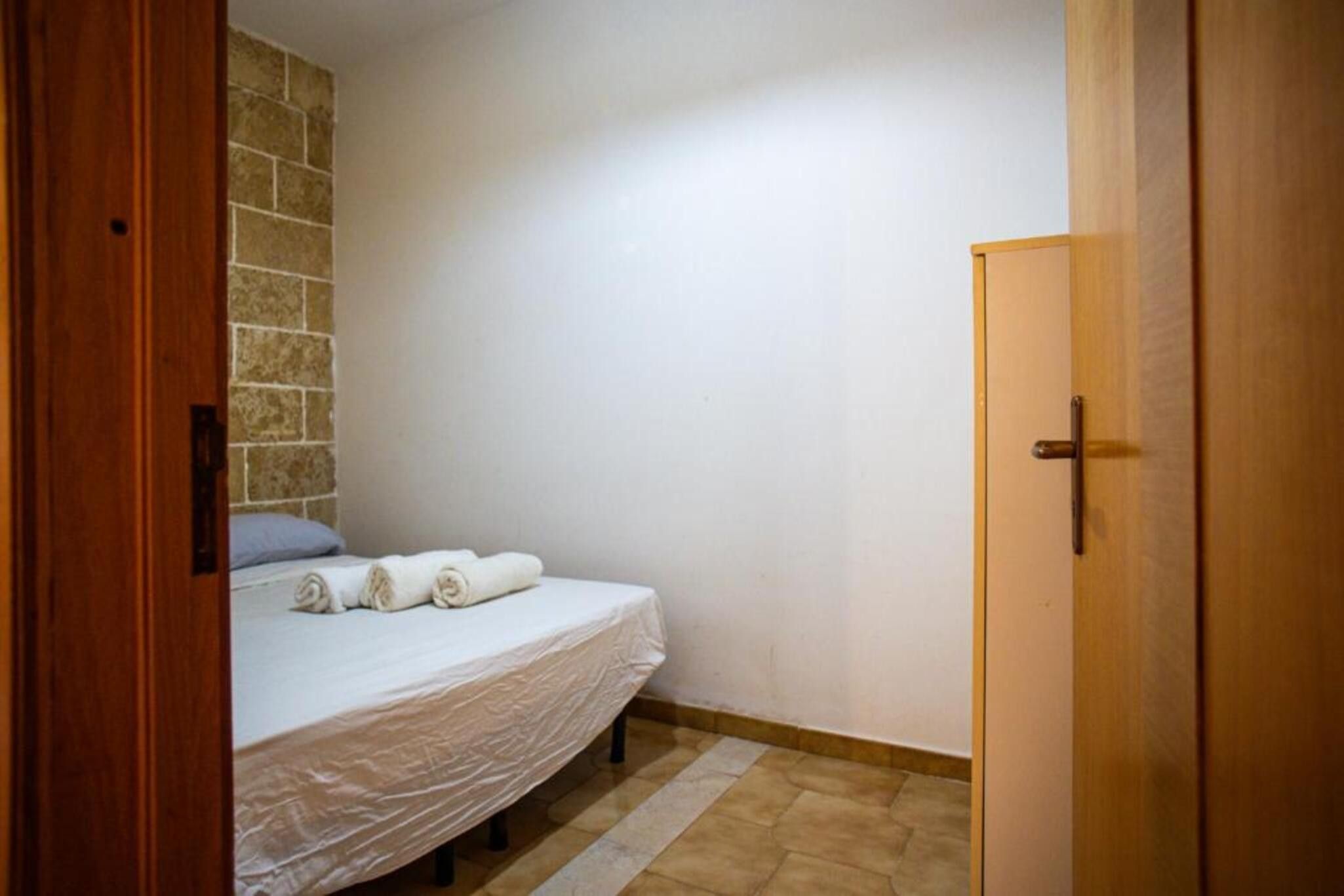 Una habitación pequeña con una cama individual, puerta de madera y pared de piedra.