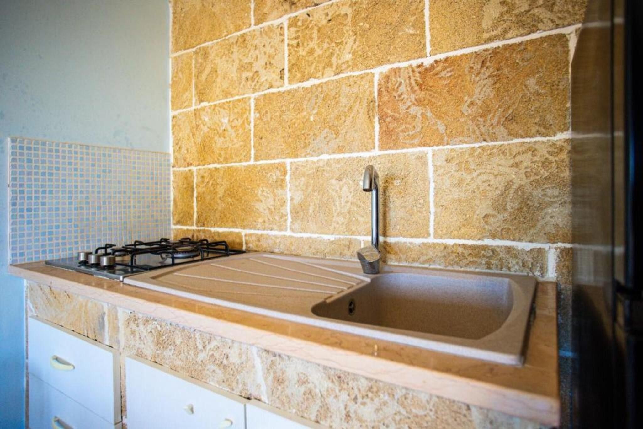 Une cuisine équipée d’une cuisinière à gaz, d’un évier et d’un plan de travail recouvert de carreaux.