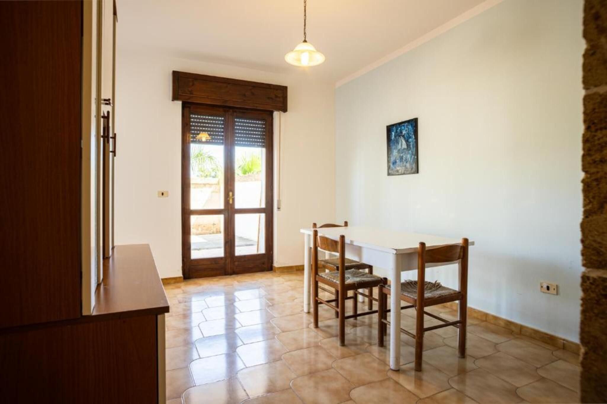Una habitación con una mesa de comedor de madera y sillas, una lámpara colgante y una puerta con ventana.