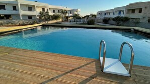 A swimming pool with a wooden deck and metal ladder, surrounded by modern buildings with white facades. - Apartment 'Residence Eriguez - 8' with Shared Pool, Wi-Fi and Air Conditioning (Marina di Mancaversa)