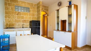 Cocina compacta con salpicadero de piedra, un refrigerador negro y una mesa de comedor blanca con sillas.