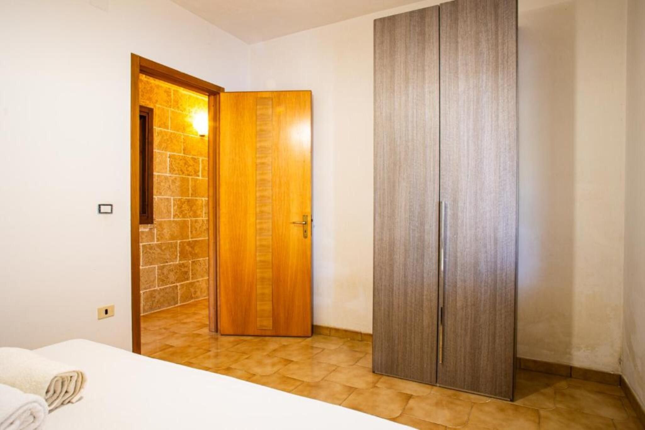 A room with a bed, a wooden wardrobe, and a door leading to another room.